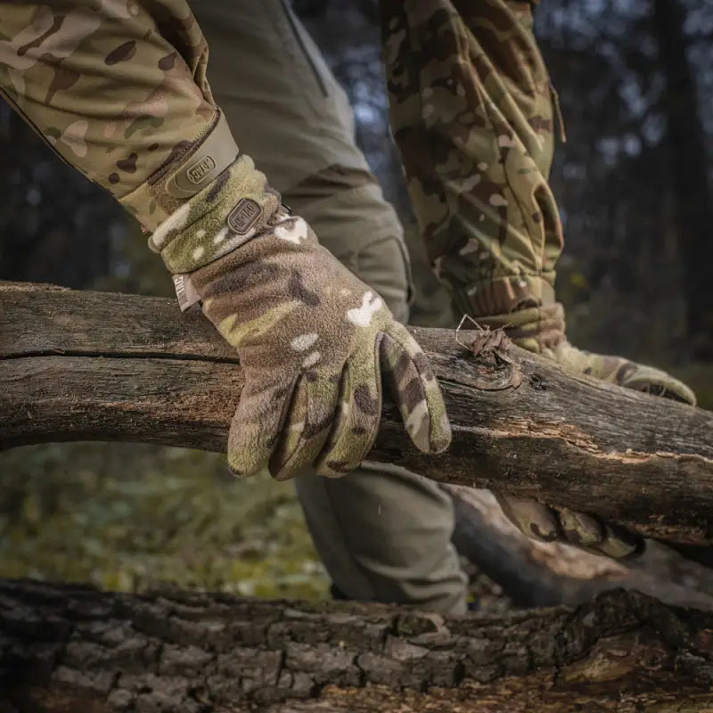 Camouflage-patterned M-Tac Gloves Fleece Thinsulate gripping a fallen tree branch