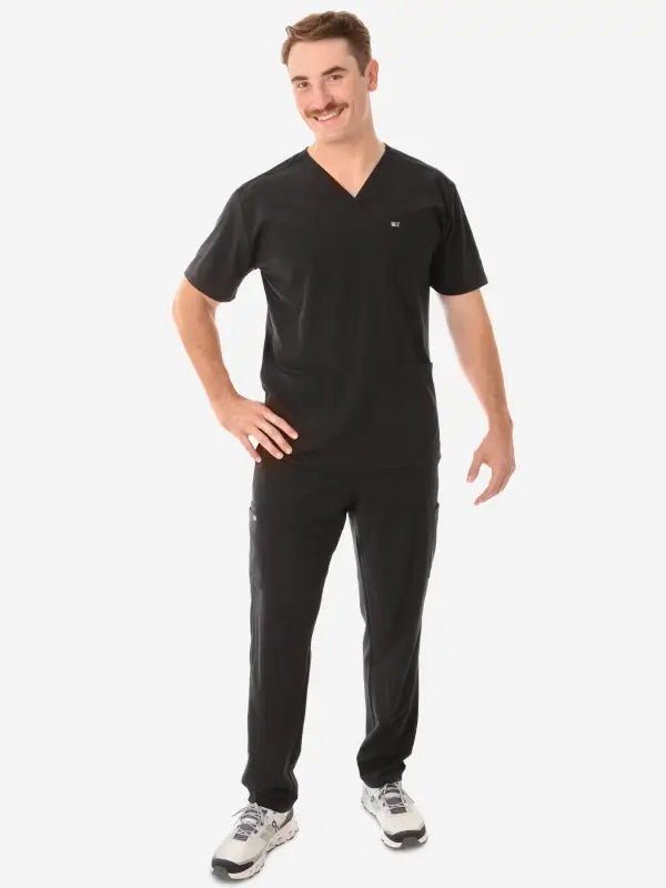 Black v-neck Men’s Five-Pocket Scrub uniform with matching pants and gray sneakers