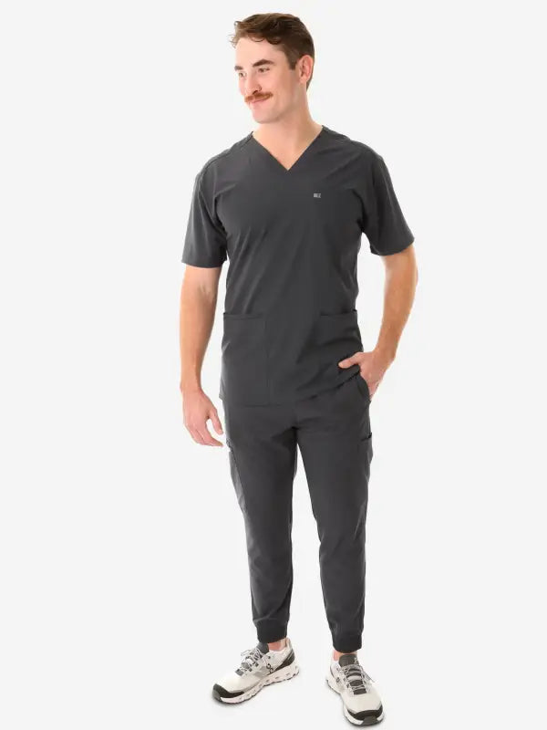 Dark gray men’s five-pocket scrub set with jogger-style pants and sneakers