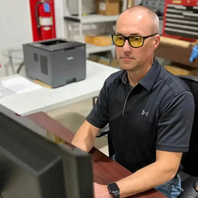 Person in dark Under Armour polo wearing METEL M40 safety glasses at a desk