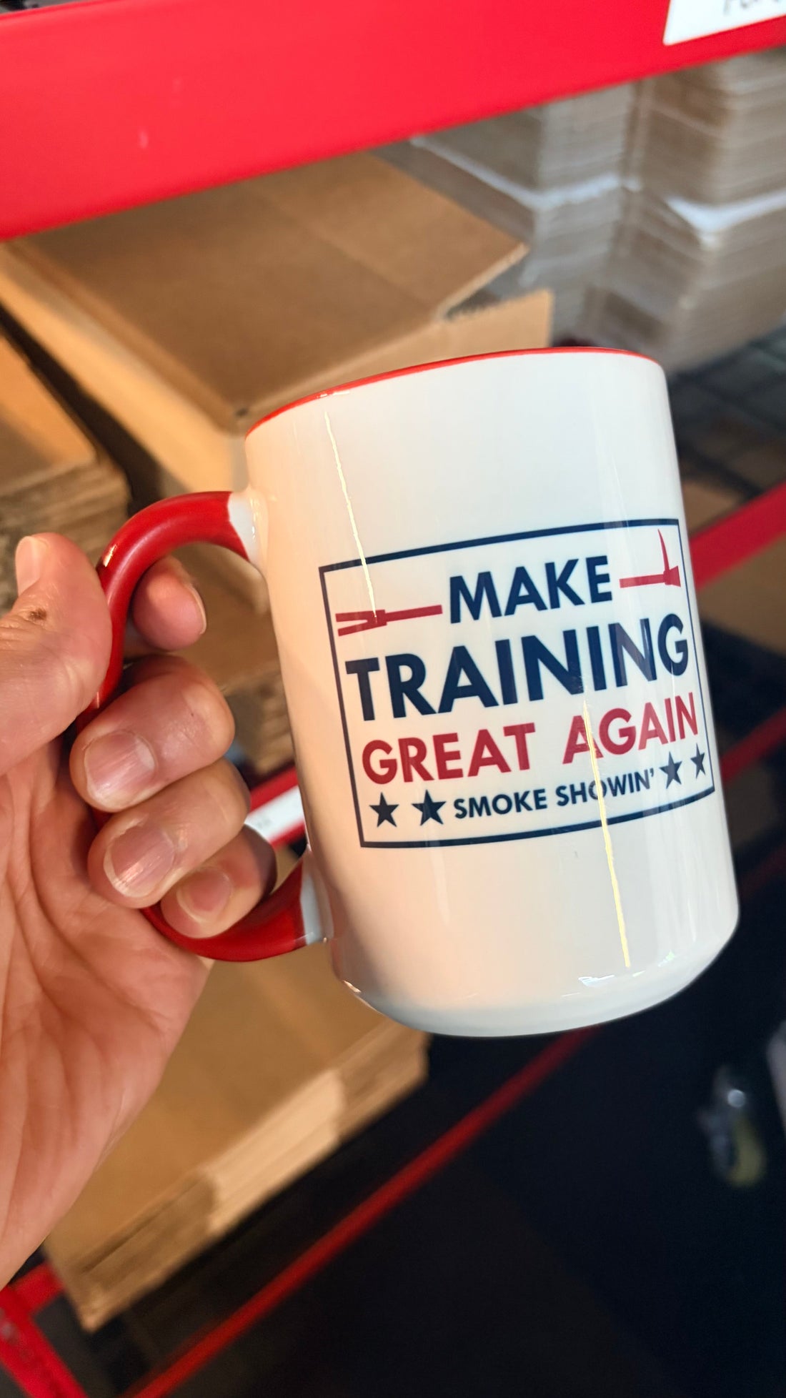 Mug with 'Make Training Great Again' text held by a hand in front of a red and black background.