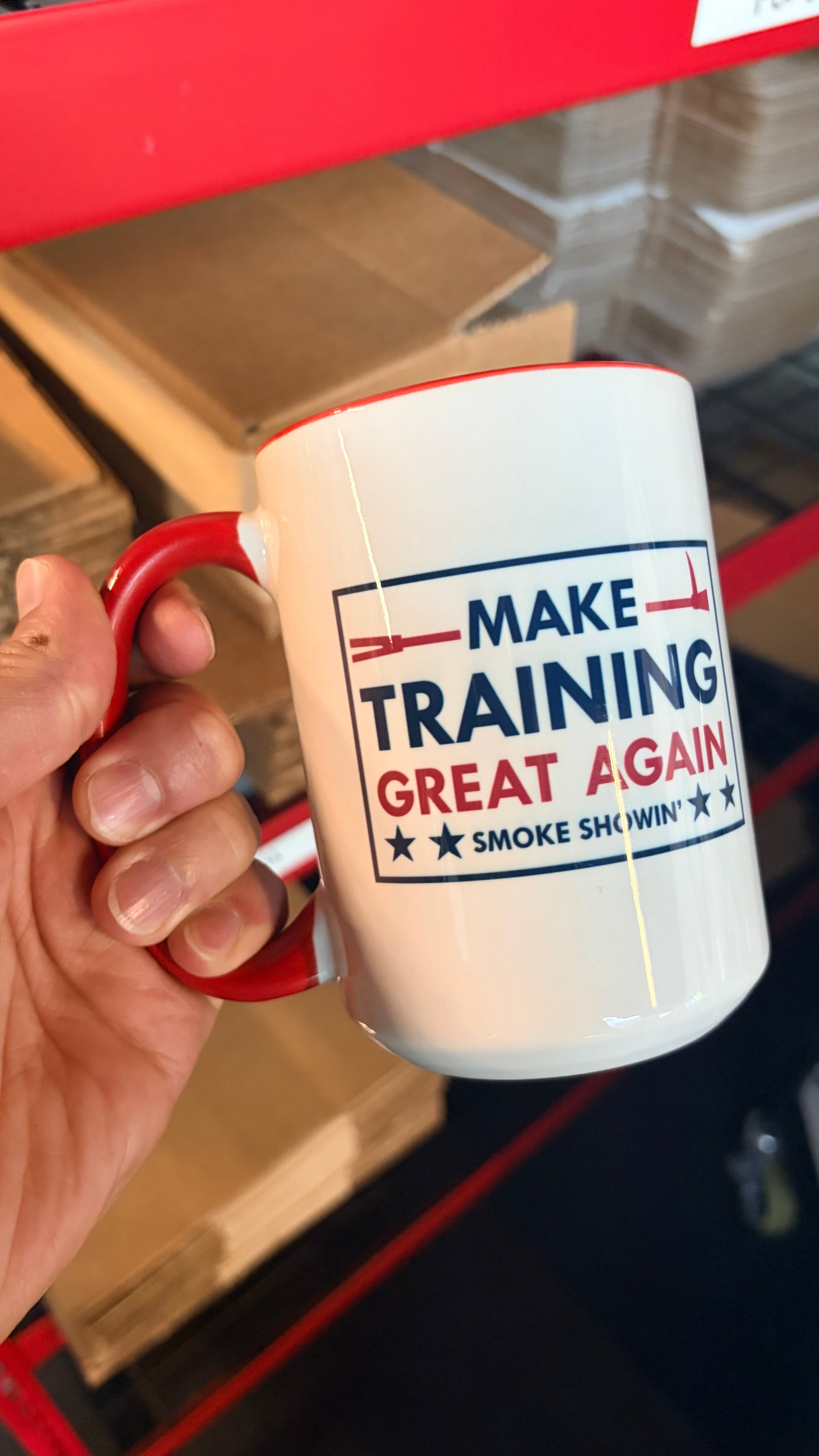 Mug with 'Make Training Great Again' text held by a hand in front of a red and black background.
