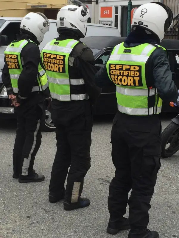 Three motorcycle escorts in high visibility vests stand in a line showcasing ANSI II Cert