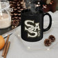 Black ceramic mug with SA logo steaming, showcasing the Letter Stack Mug design