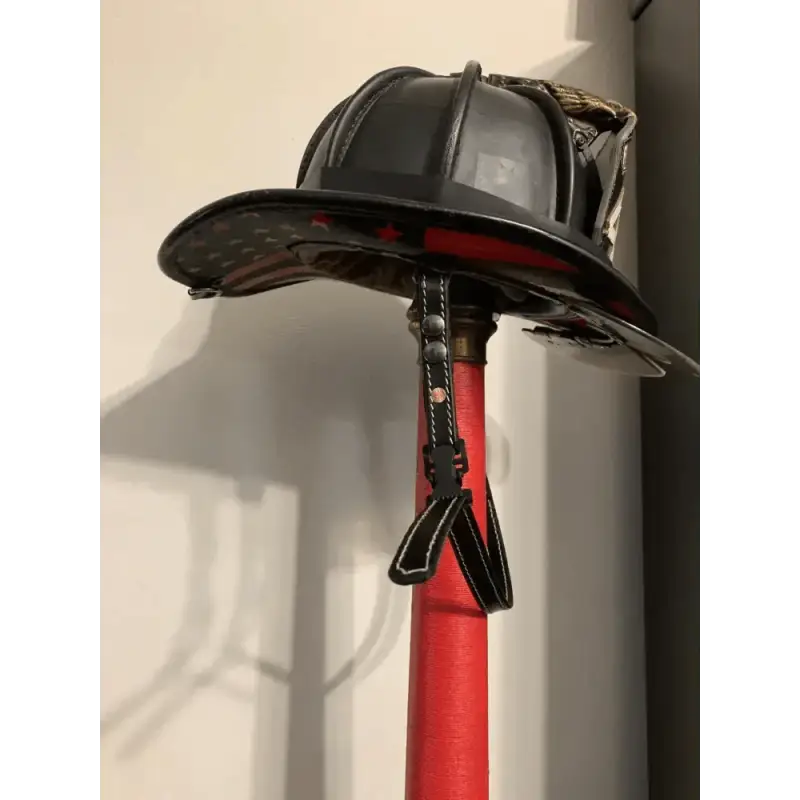 Black firefighter helmet on red pole featuring smooth leather chin straps for durability