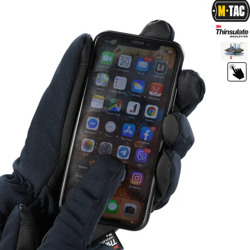 Black gloved hand holding an iPhone with apps, showcasing M-Tac Gloves Soft Shell Thinsulate