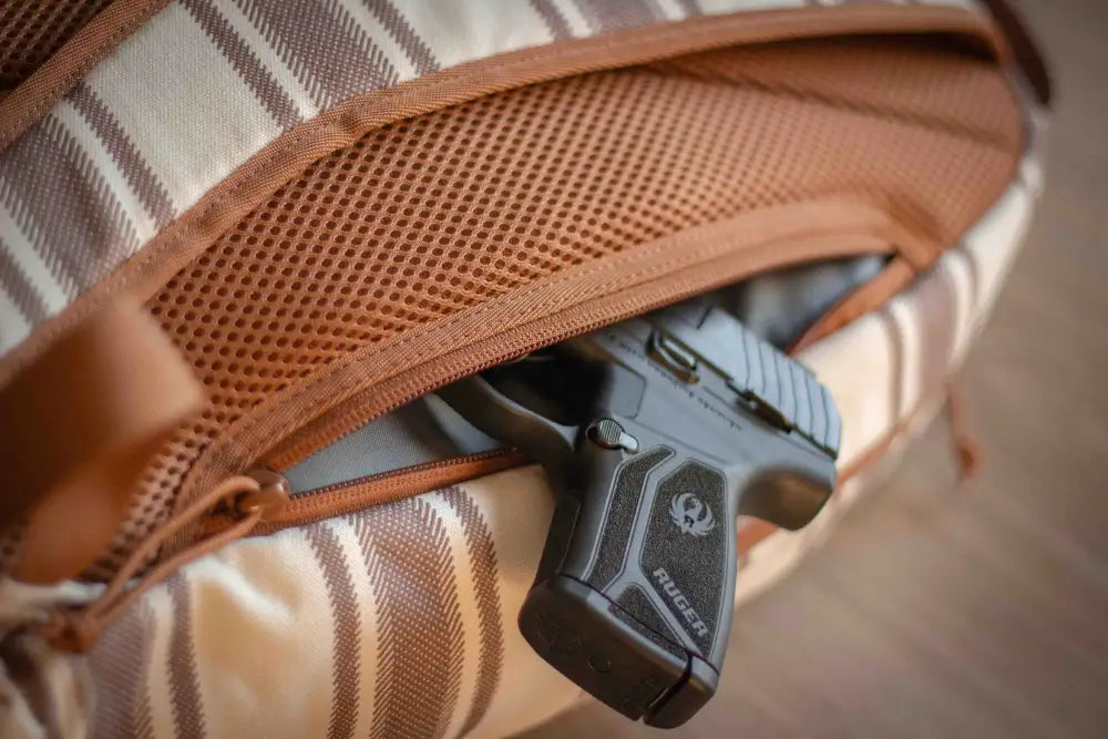 Black handgun in brown mesh holster inside ECHO EDC Backpack for concealed carry