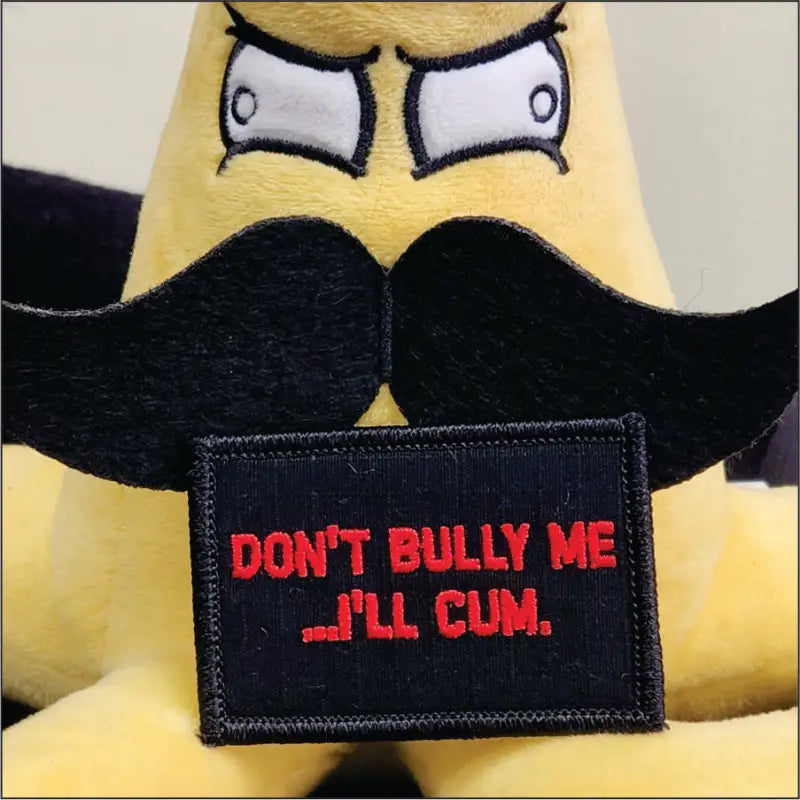 Black w red patch reading Don’t Bully Me I’ll Cum on a yellow plush toy with mustache