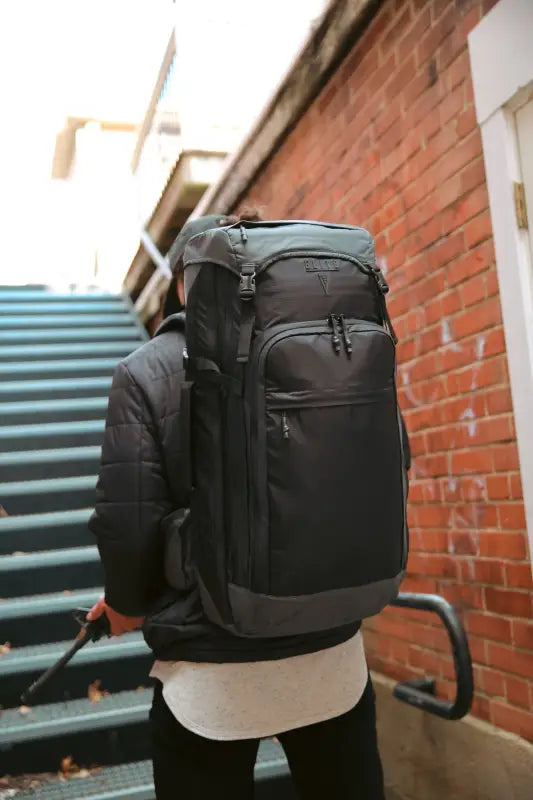 Black tactical backpack with compartments and adjustable tie-down for discreet rifle storage