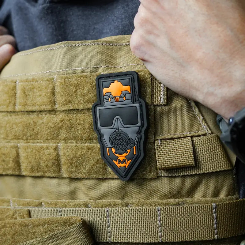 Black PVC morale patch with orange skull design on tan MOLLE webbing