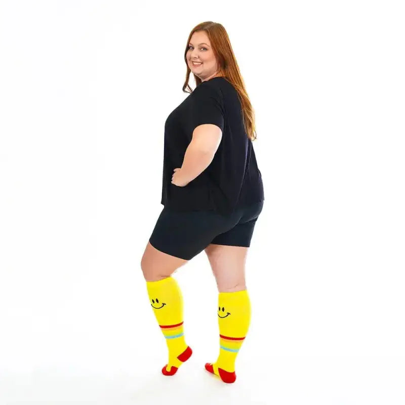 Bright yellow Marathon Wide-Calf socks with smiley faces complement a stylish black outfit