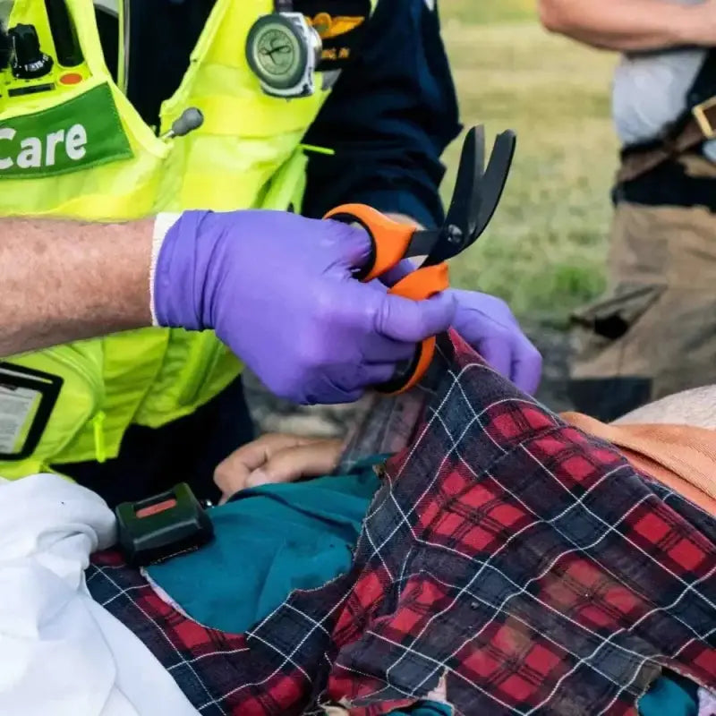 Emergency worker in safety vest using trauma shears with black titanium coated blades