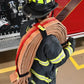 Firefighter carrying coiled fire hose with Adjustable Hose Bundle Strap Kit in Red