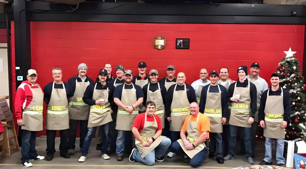 Group of people in matching tan aprons by a Christmas tree showcasing personalized black cooking