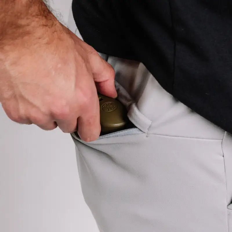 Hand placing a brass padlock in a pocket of Carrier Shorts with patented carrier retention