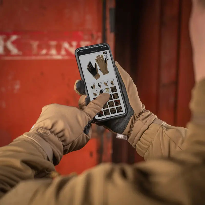 Hands in brown M-Tac Gloves Soft Shell Thinsulate holding a smartphone with an app