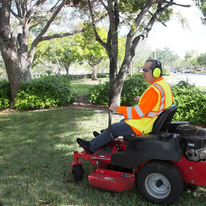 Operator using 27dB NRR noise cancelling hearing protection earmuffs on a riding lawn mower