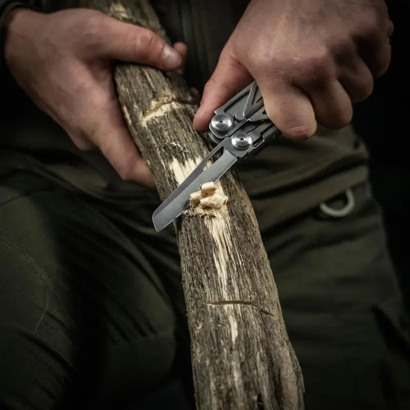 A M-Tac Multitool Type 3 Grey used to whittle wood, showcasing its versatile design