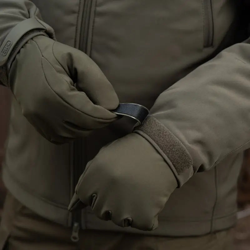 Black ring held by gloved hands near M-Tac Soft Shell Jacket with two shoulder pockets