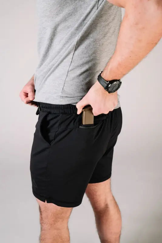 Man in black athletic shorts showcasing Carrier Shorts Mk.II for concealed carry