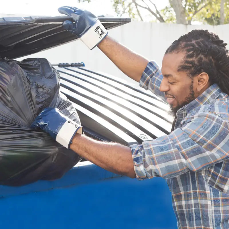 Man in Fully Coated Nitrile Safety Work Gloves tossing trash bag into dumpster