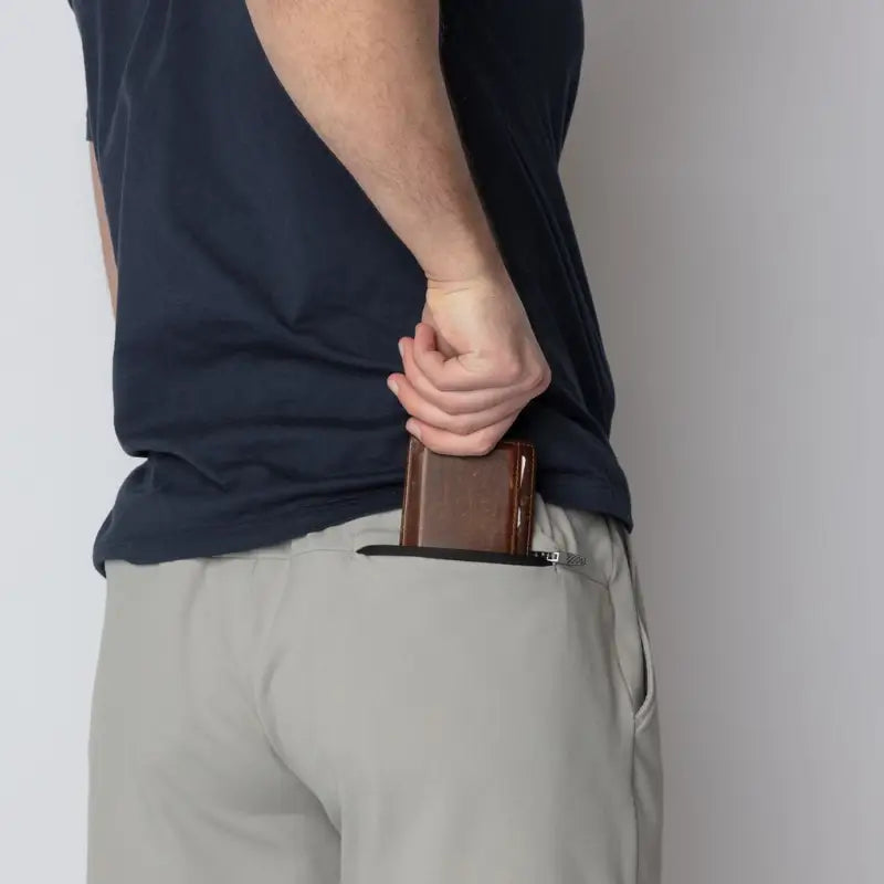 Man wearing Carrier Shorts Mk.II for concealed carry, placing wallet in zippered pocket