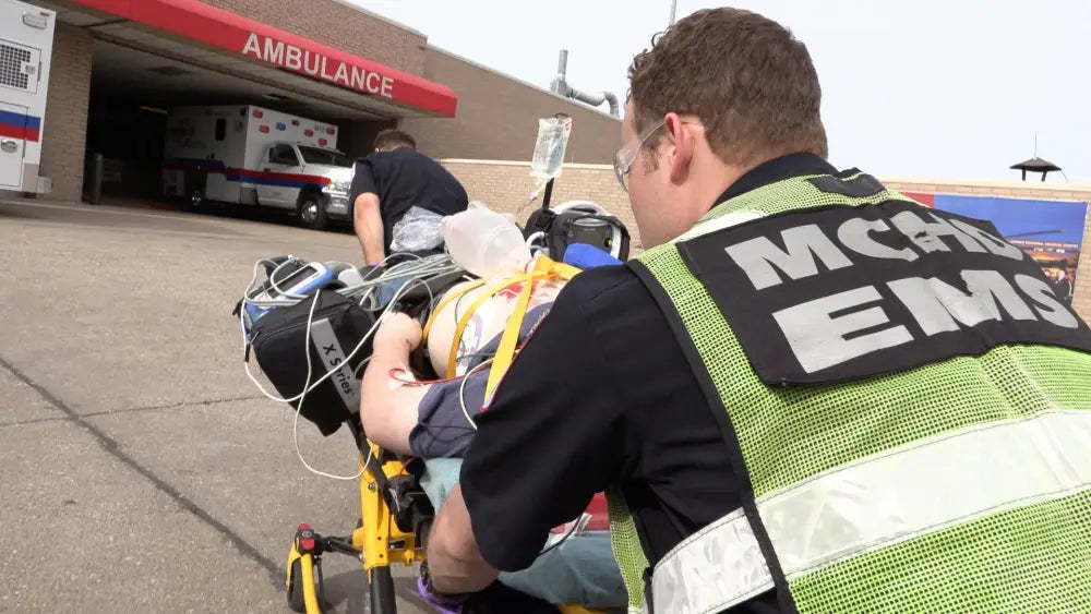 EMT personnel using MCHD ANSI II Adjustable Vest transport patient to an ambulance bay