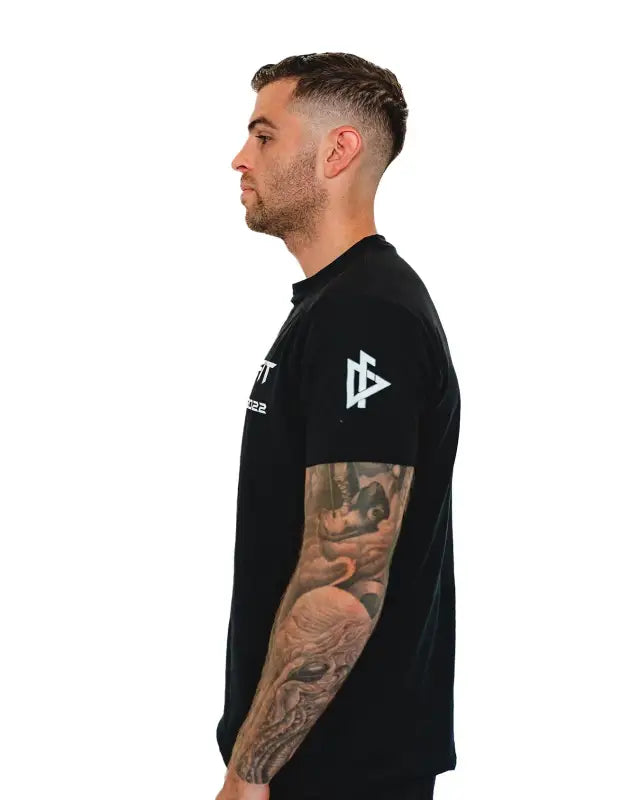 Black Men’s Gym Tee Compellence with white geometric logo and visible arm tattoo