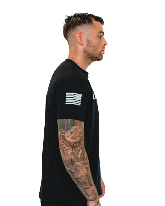 Side view of Men’s Gym Tee Compellence featuring American flag patch and arm tattoos