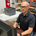 Person in dark Under Armour polo wearing METEL M40 safety glasses at a desk