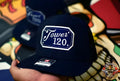 Navy blue baseball cap with Tower 120 patch and square passport cursive lettering design