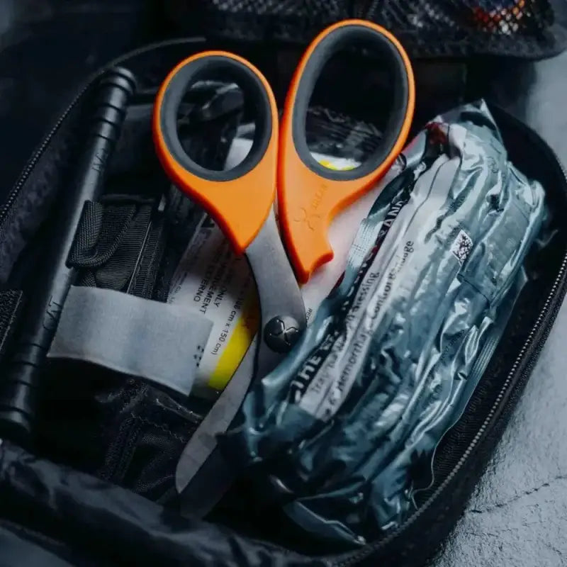 Orange-handled scissors among medical supplies showcasing XShear Trauma Shears with black titanium coated blades