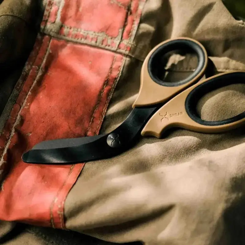 Black and gold trauma shears resting on fabric, featuring black titanium coated blades