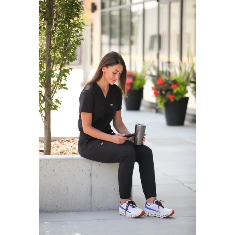 Person in black athletic wear sitting on ledge with Women’s Tuckable One-Pocket Scrub Top