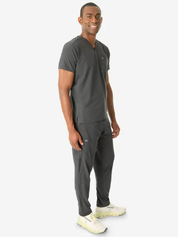 Person in dark gray medical scrubs and white sneakers wearing men’s double-pocket scrub