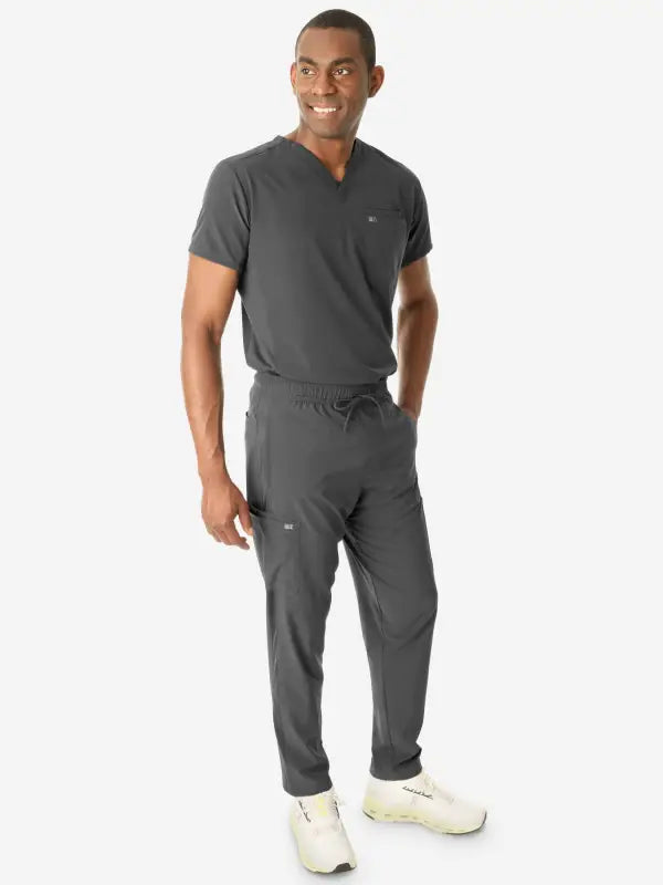 Person in gray medical scrubs and white sneakers wearing a men’s double-pocket scrub top