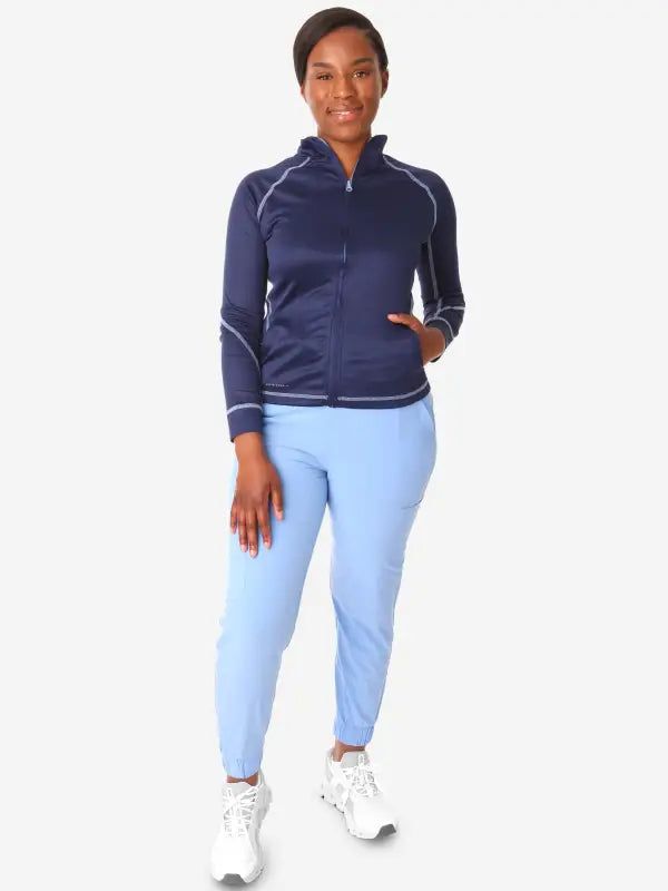 Person in navy blue women’s scrub jacket, light blue pants, and white sneakers