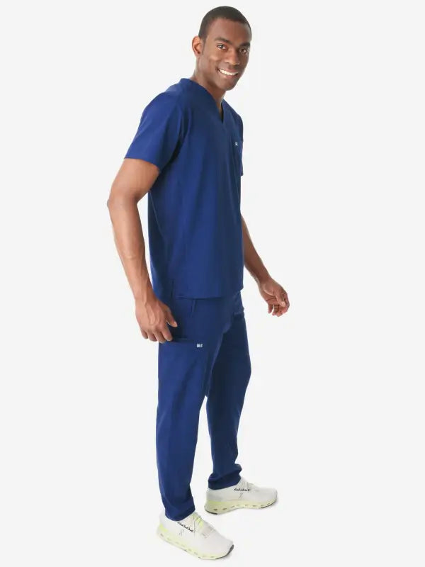 Person in navy blue medical scrubs and white sneakers showcasing men’s double-pocket scrub