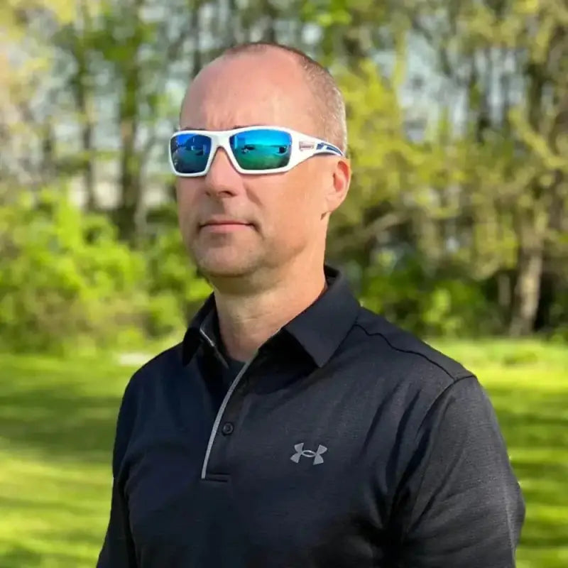 Person in white-framed sunglasses with blue mirror lens wearing black Under Armour polo shirt