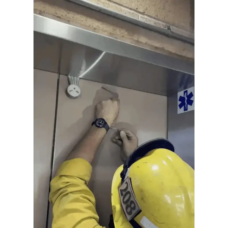 Person in yellow safety gear working on elevator control panel for Williams Wedge