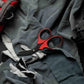 Red-handled trauma shears on dark fabric, featuring black titanium coated stainless steel blades