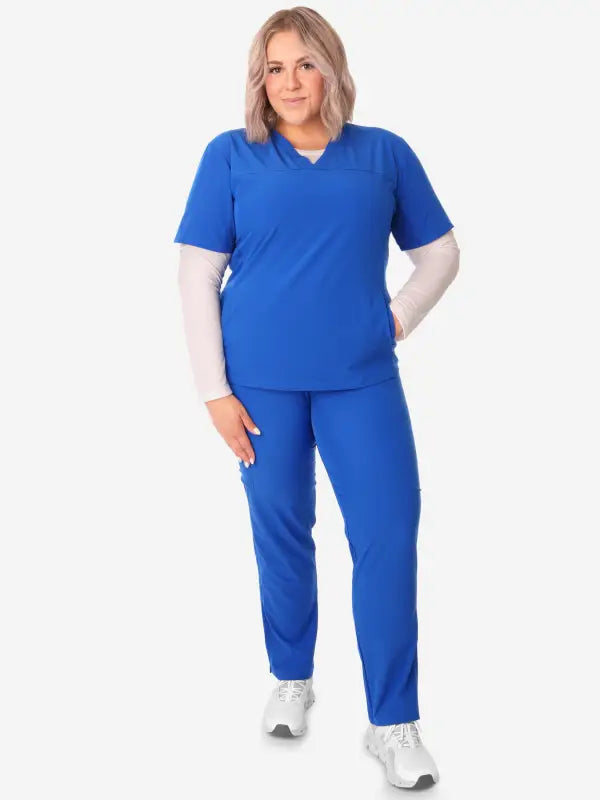 Royal blue women’s stash-pocket scrub top with white undershirt and sneakers