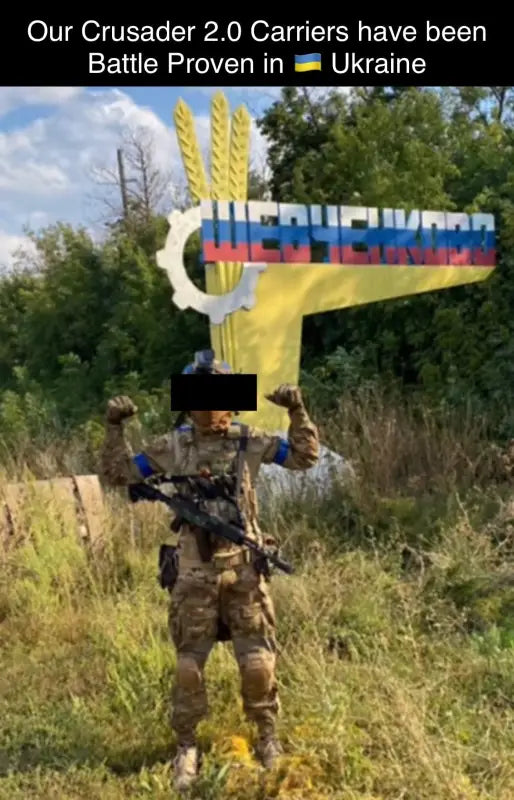 Soldier in camouflage body armor with assault rifle and medical kit in front of a sign