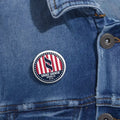 Circular red, white and black Stars and Stripes pin button on denim fabric