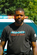 Person in a black Stigma-Breaking Unisex Tee supporting mental health by a police vehicle