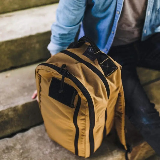 Tan canvas backpack with black trim, featuring 12HR Plus Royal Blue and 1000D Cordura