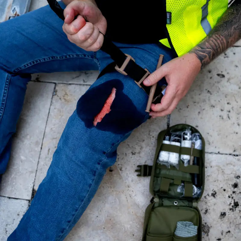 Torn jeans with injury visible, showcasing The First Responder IFAK Kit in action