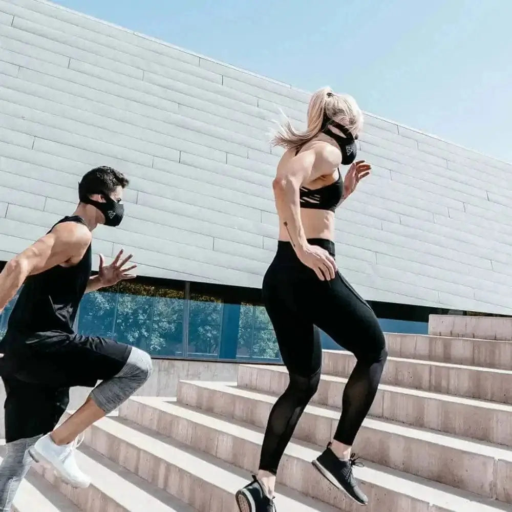 Two people in black training masks running up concrete steps for endurance training