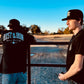 Two people in black staple tees by a railing, one featuring RUST & IRON text