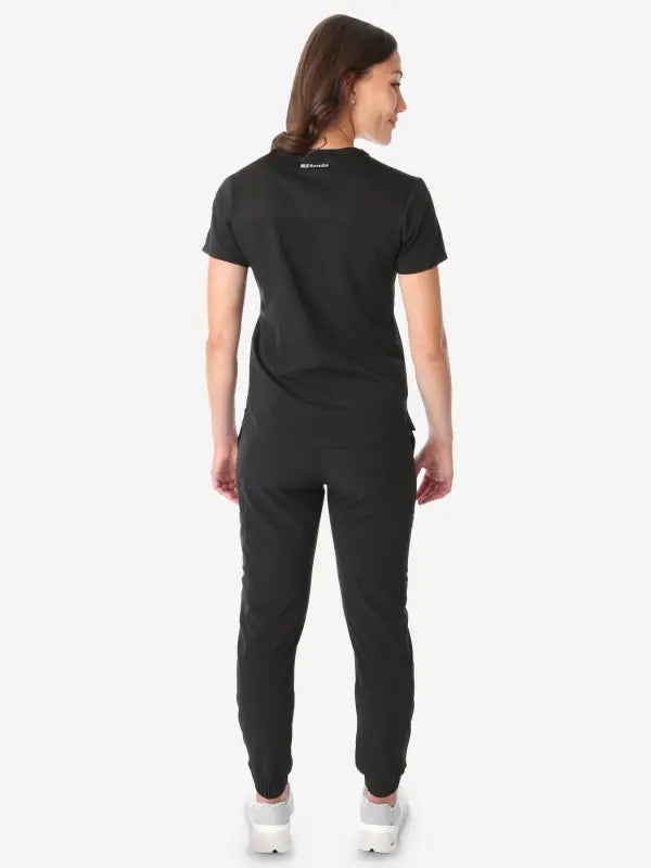 Back view of model in a Women’s Tuckable One-Pocket Scrub Top, joggers, and sneakers